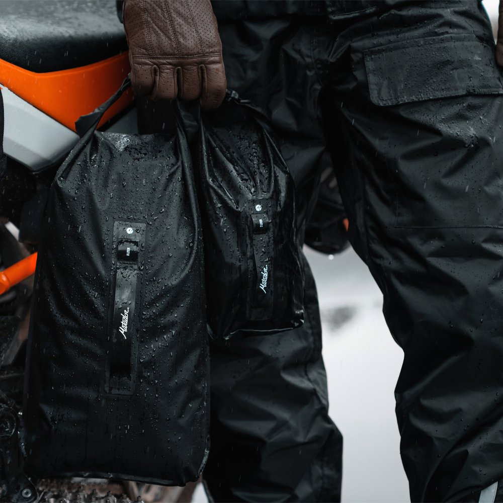Man standing by motorcycle, holding rain covered 2L and 8L dry bags