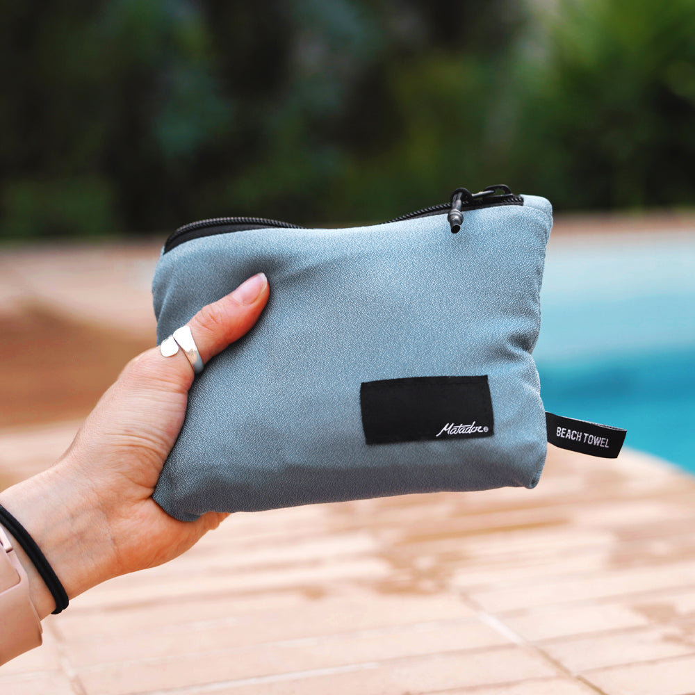 Hand holding out packed up slate blue towel in front of pool