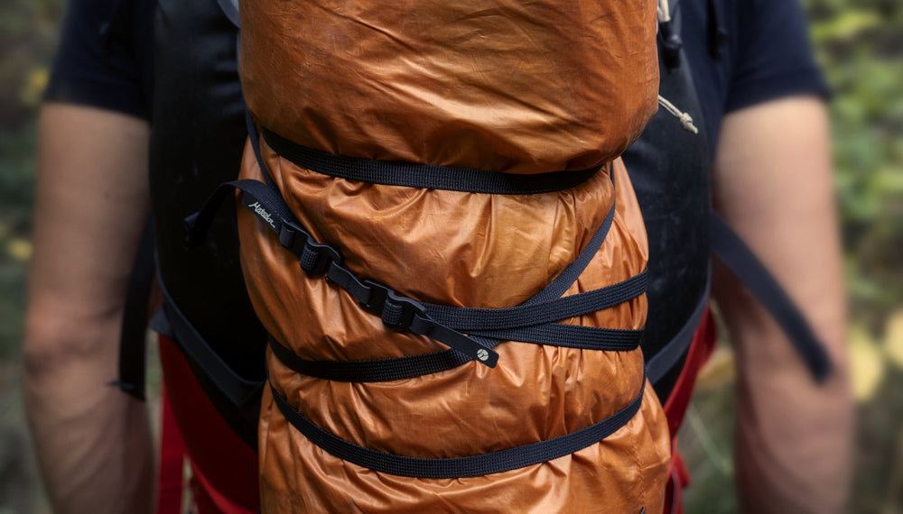 Man wearing backpack with orange tarp attached with Better Tether