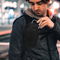Man in city at night, pulling phone out of Speed Stash on backpack strap