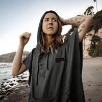 tattooed woman on beach wearing charcoal poncho