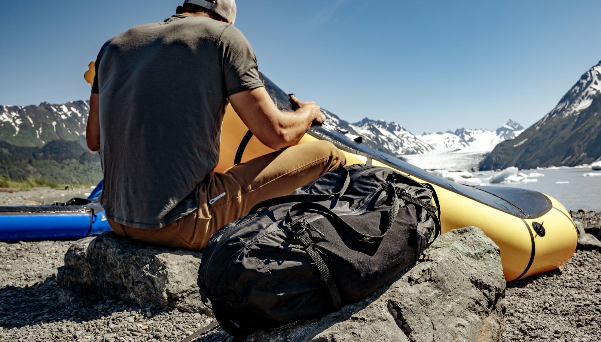 Man on shoreline with yellow, inflatable kayak with black duffle sitting next to him