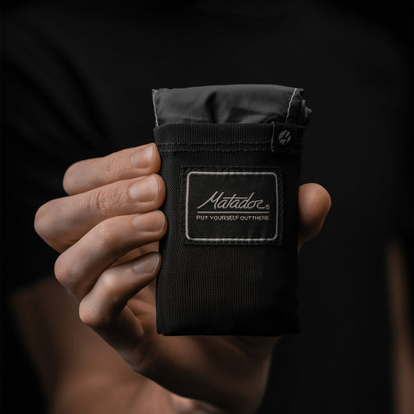 Hand holding packed down pocket blanket on black background