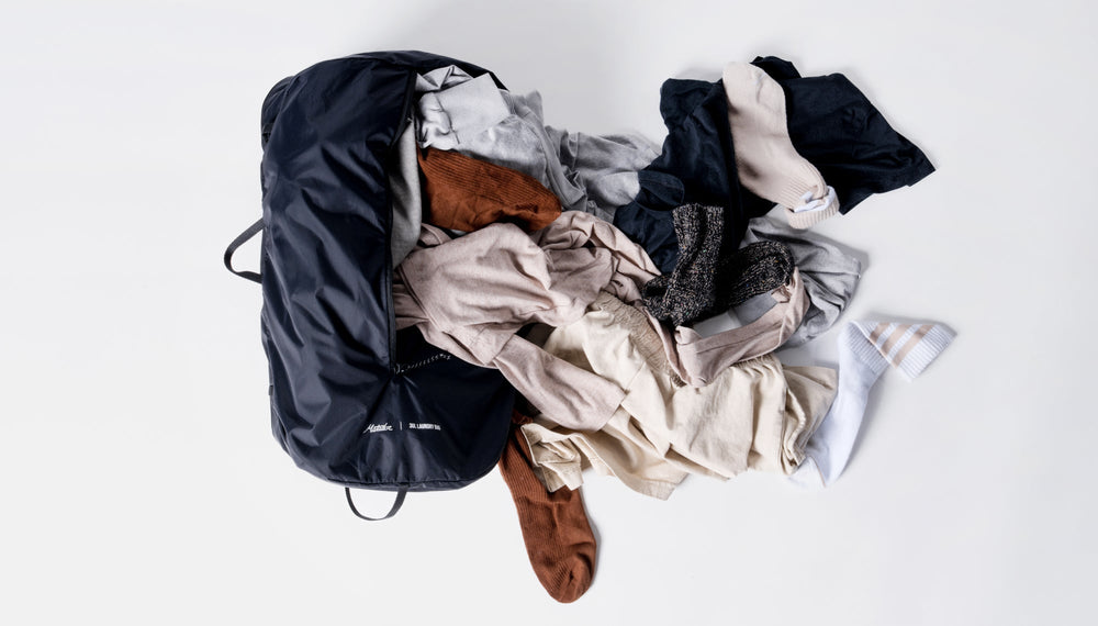 Laundry bag laying on white background with dirty laundry spilling out of the large side zipper