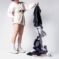 woman standing in white studio background, dumping clothing out of laundry bag by holding the bottom grab handle