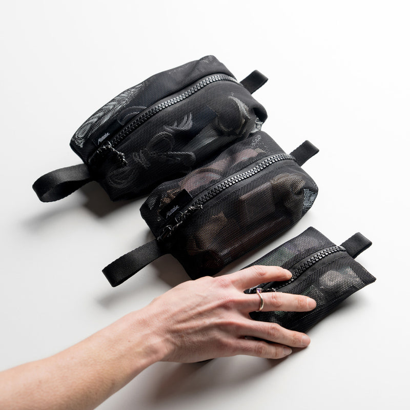 woman's hand grabbing the smallest of 3 mesh bags, all full with items