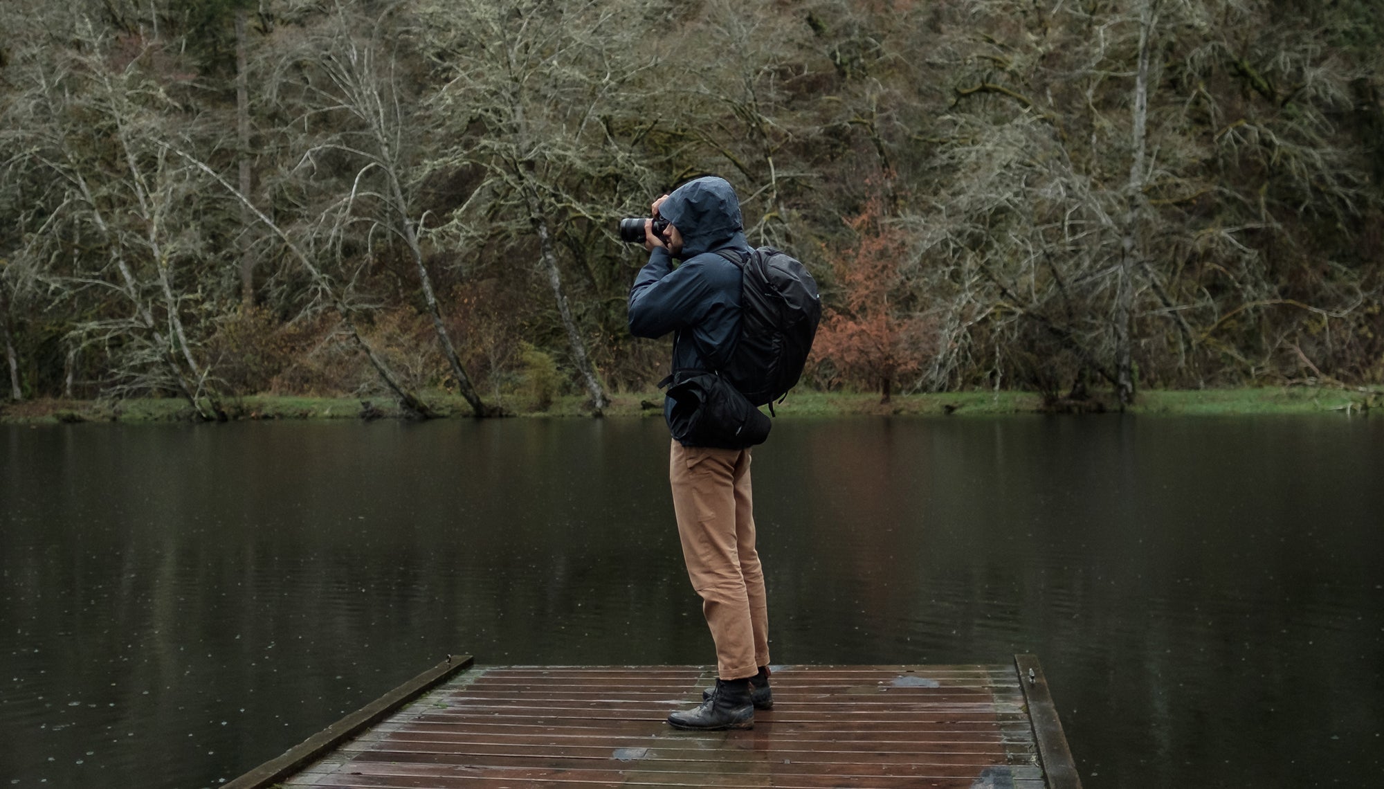 Man on rainy lake dock, taking a photo