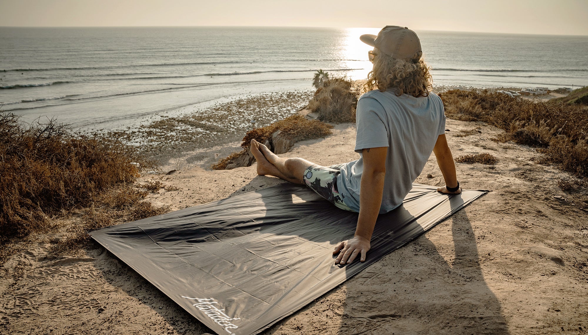 Man on sandy, sunset coastline, sitting on pocket blanket